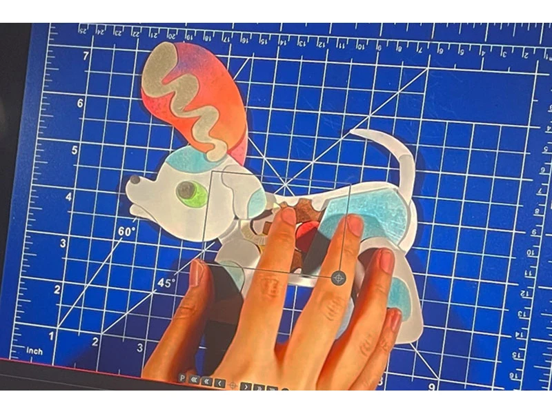 Colorful dog puzzle on a blue grid cutting mat with hands arranging the pieces.