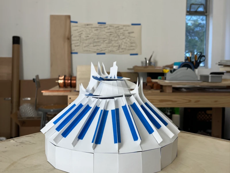 Paper model of a dome with blue stripes on a wooden table in a studio environment.