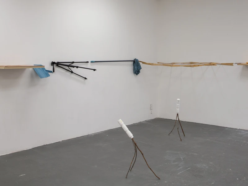 Art installation with various objects attached to a horizontal line on white walls and minimalist sculptures on the floor.