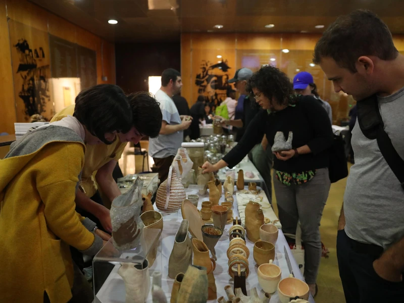 People examining ceramic objects on a display table in an indoor setting.
