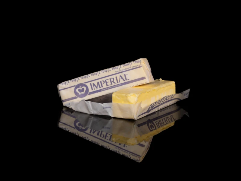 Stick of Imperial butter partially unwrapped on a reflective black surface.