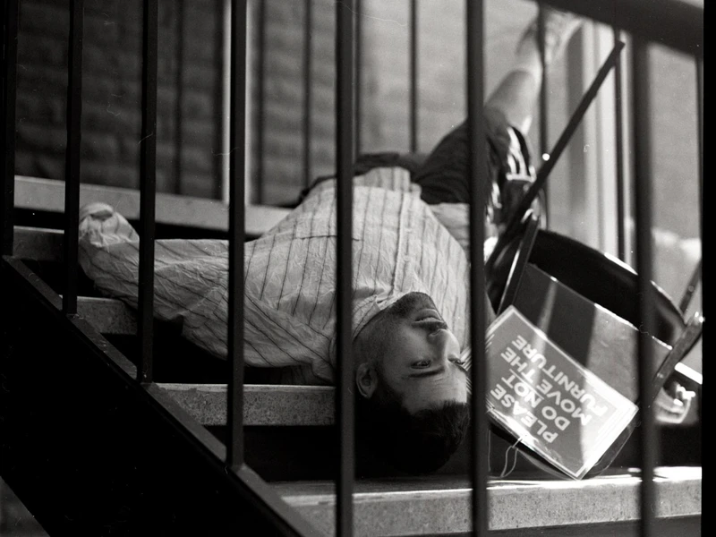 A man lying across a staircase with an overturned chair beside him.