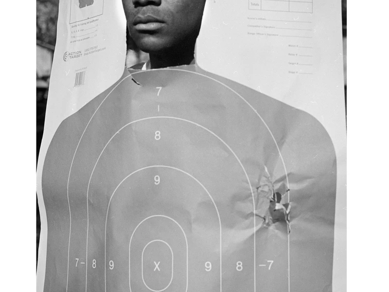 A shooting target with a man's face overlay, showing bullet holes and concentric scoring rings.