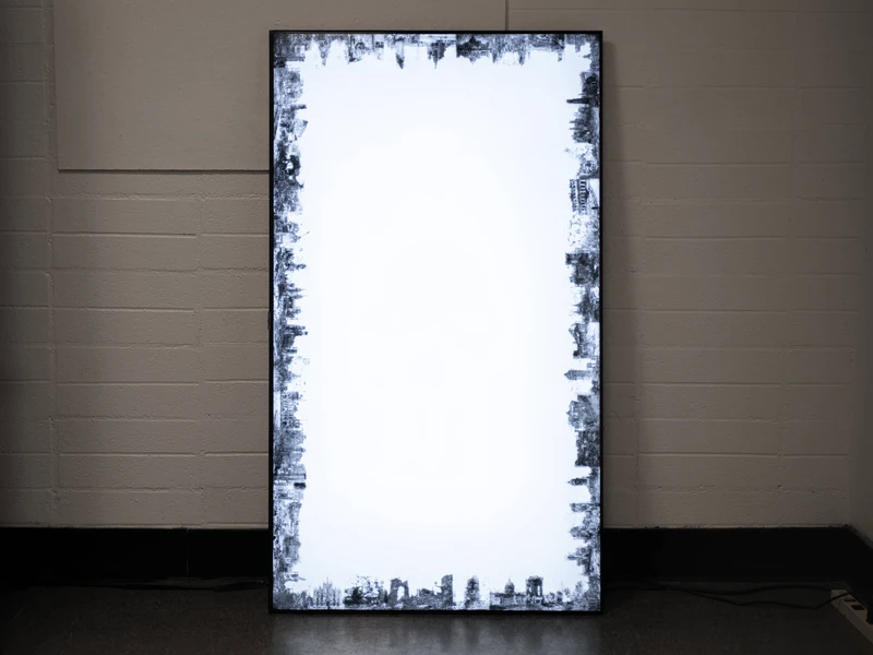 Rectangular light box with abstract black and gray skyline patterns on the edges against a white wall.