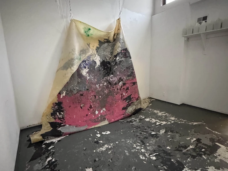 Abstract painted canvas hanging in a room with paint-splattered floor.