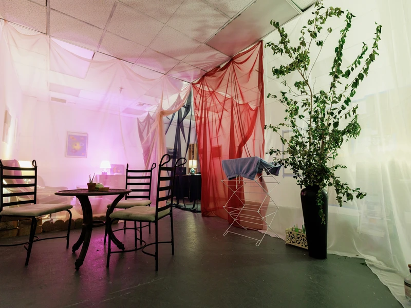 Room with round table and chairs, sheer drapes, potted plant, and ambient pink lighting.