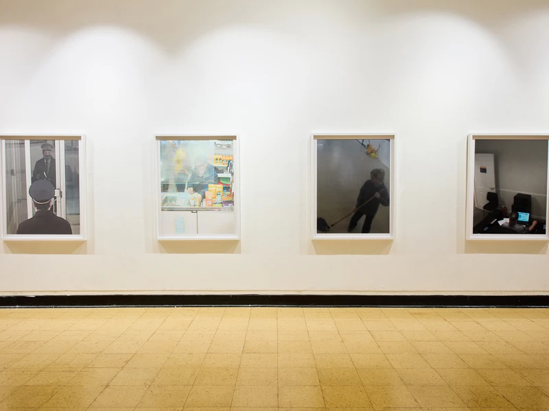 Four framed photographs hang on a white wall in a gallery, each depicting different everyday scenes.