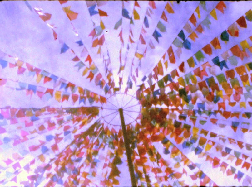View from below of colorful triangular flags radiating from a central pole against a bright sky.