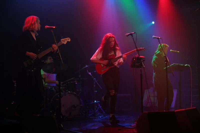 A band performing on a stage with colorful red, blue, and green lighting effects.