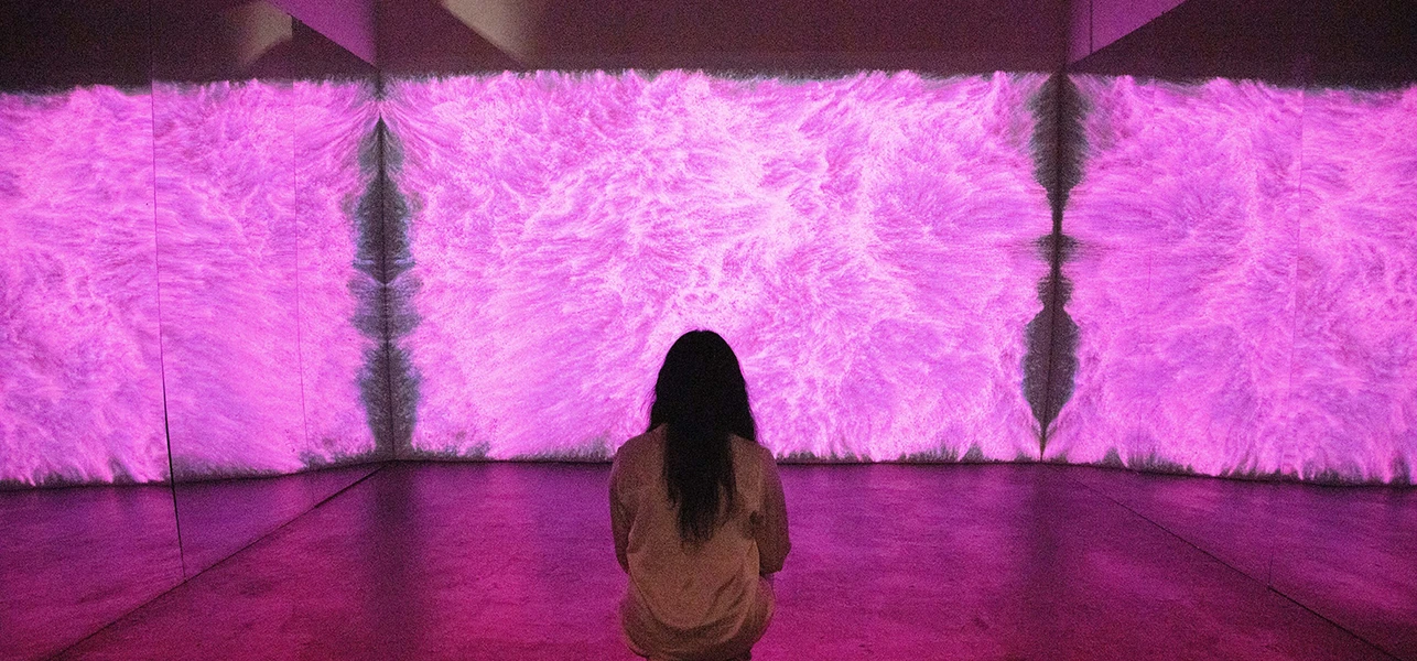 Person sitting in front of a digital art installation with swirling lavender textures.