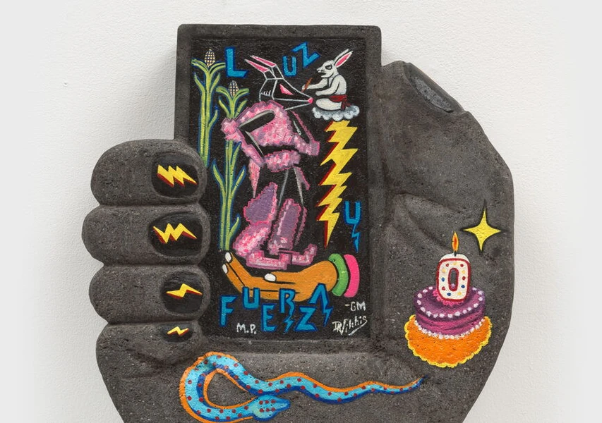 Sculptural artwork of a large hand holding a colorful frame with a rabbit, humanoid figure, lightning bolts, and a cake with a candle.