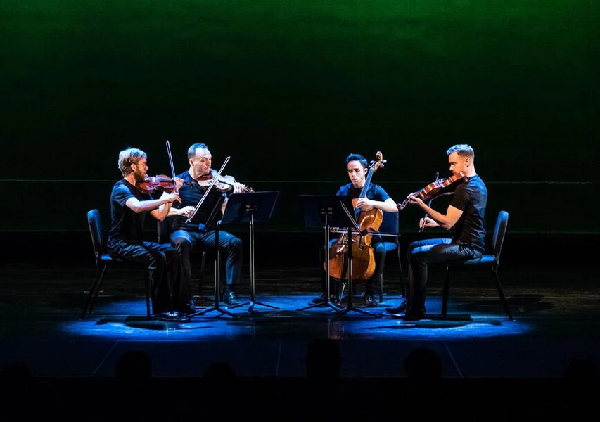 A string quartet performs under green stage lighting.