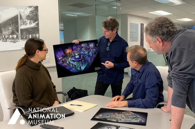 A man holds a rendering while a woman to his right in glasses and two other men at his left look on with interest.